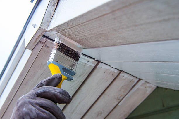 Man is painting a house with a wide brush.